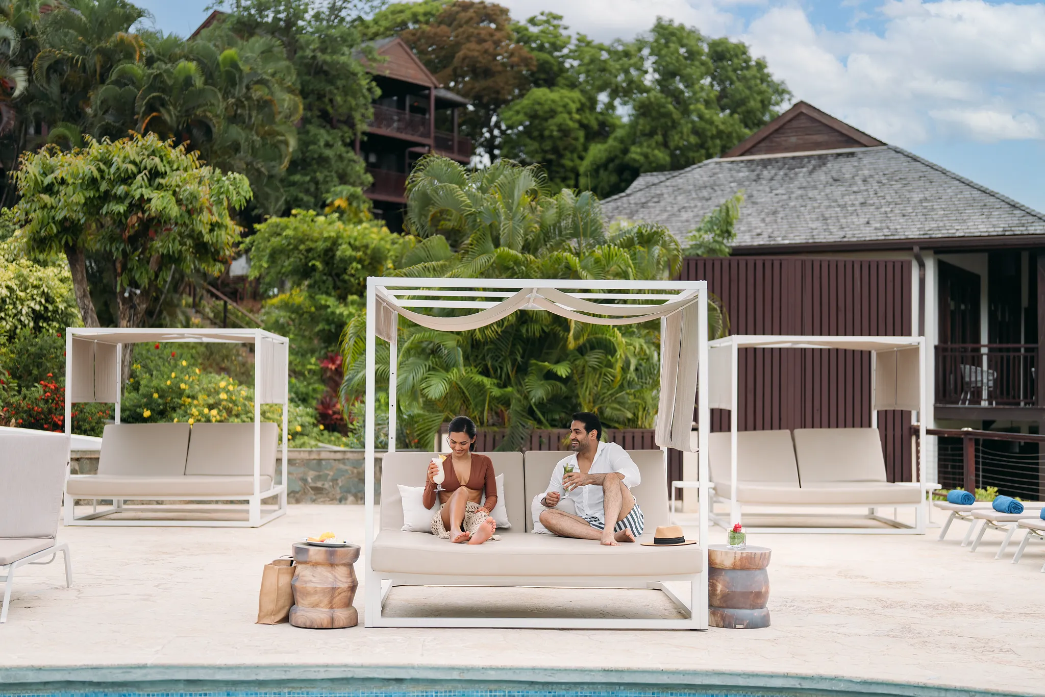 Couple relaxing on a private Bali bed with cocktails by the pool at Zoëtry Marigot Bay St. Lucia.