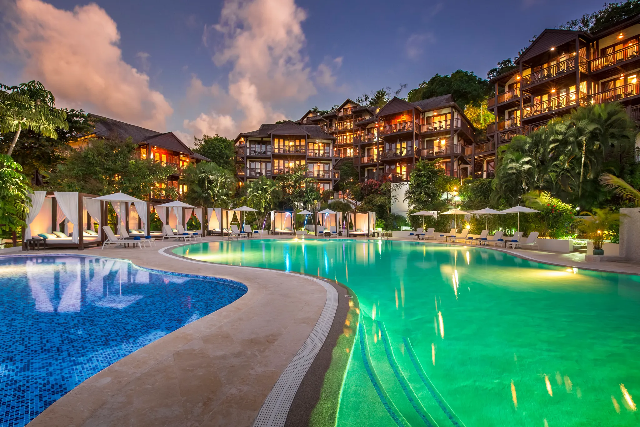 Illuminated lagoon-style pool at Zoëtry Marigot Bay St. Lucia at night with hillside suites glowing above.