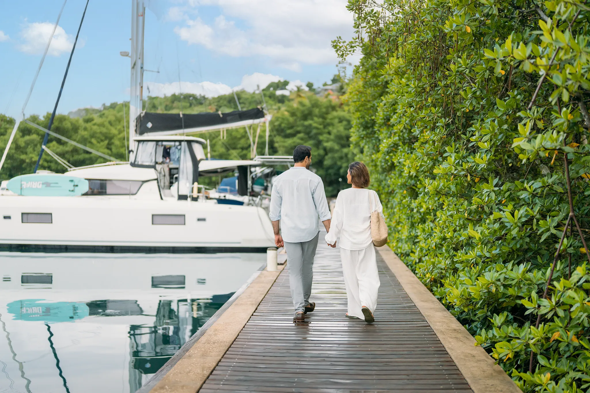 Couple strolling hand-in-hand along the marina boardwalk at Zoëtry Marigot Bay St. Lucia near luxury yachts.