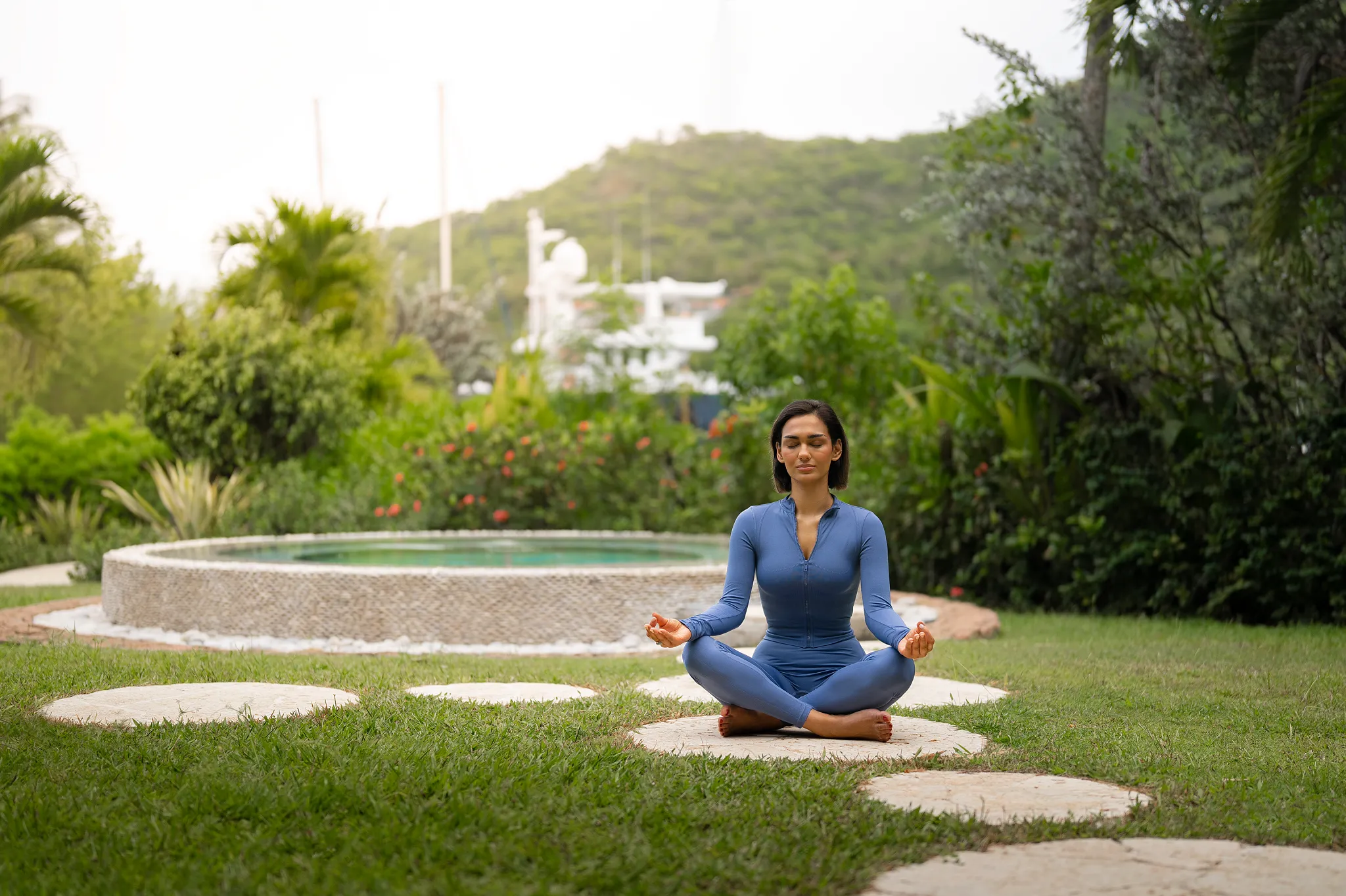Woman meditating in a lush tropical garden at Zoëtry Marigot Bay St. Lucia with marina views in the distance.
