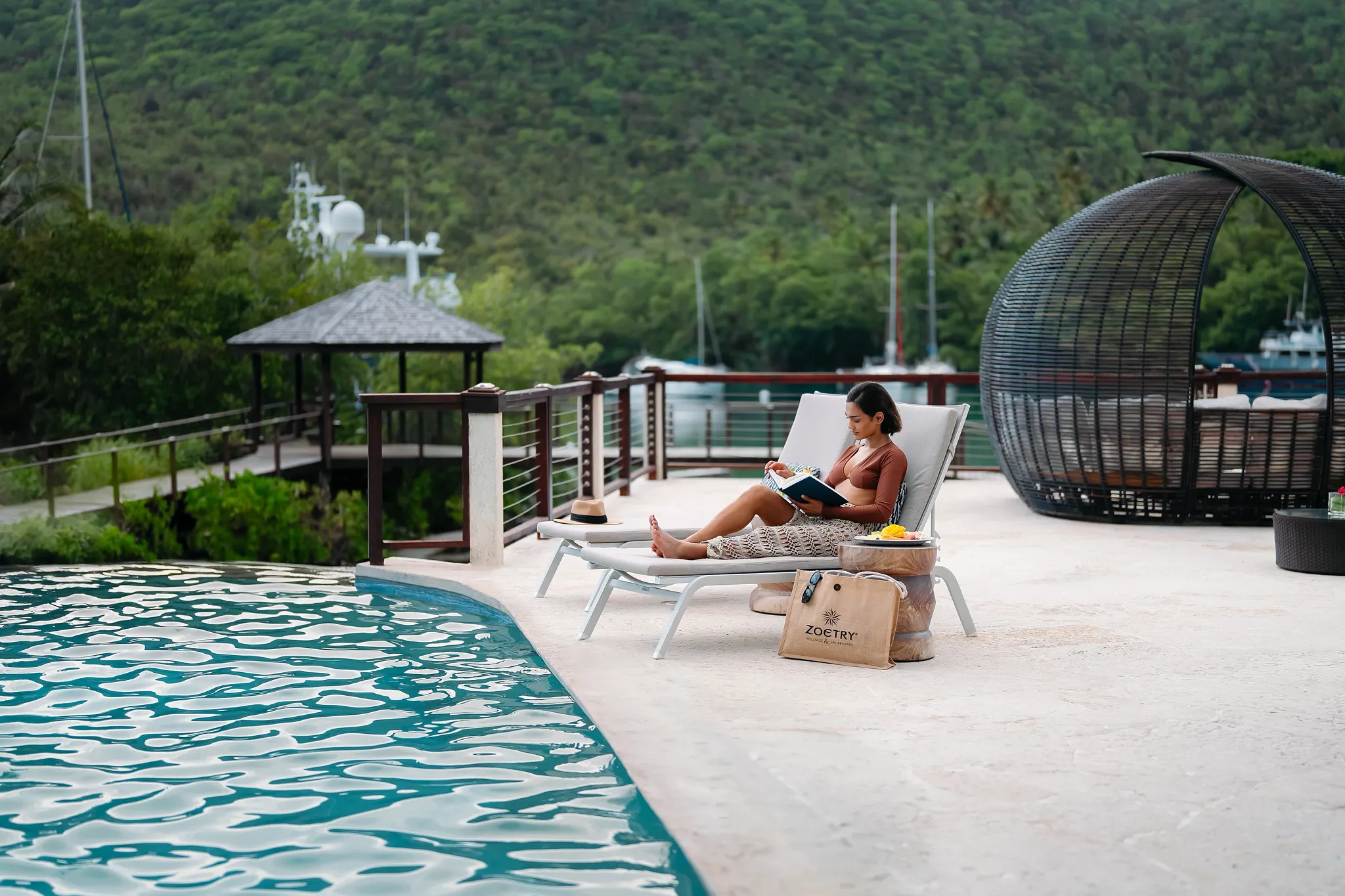 Woman reading on a lounge chair by the pool at Zoëtry Marigot Bay St. Lucia with marina views in the background.